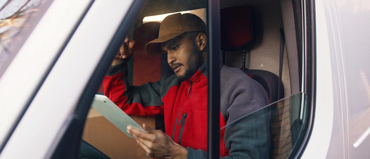 Man in driver's seat of parked delivery vehicle looking at tablet screen