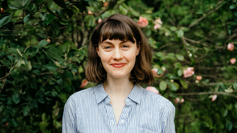 Oregon State student Ali Lanenga stands in front of green hedges while smiling.