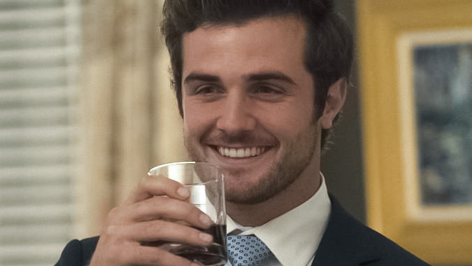 Actor Beau Mirchoff smiles while holding a glass of alcohol near his face in a scene from the TV show "Good Trouble."