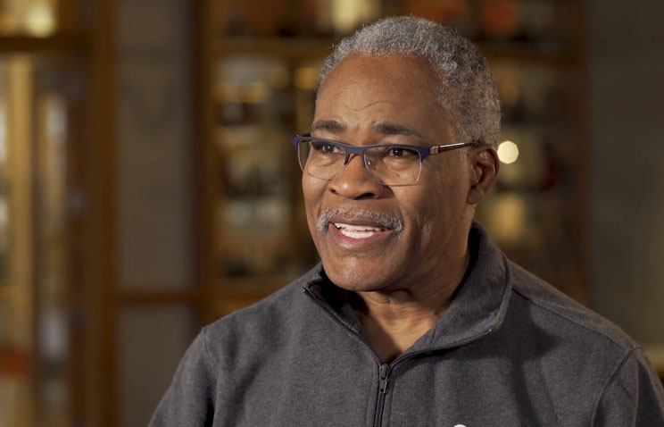 Larry Roper, director of the college student services administration program. Larry is in the middle of speaking; he wears rectangular-framed glasses and a grey quarter-zip pullover sweater.