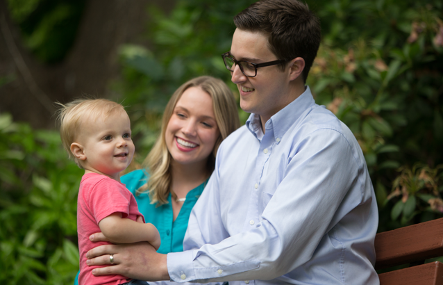 Eric Broadfoot sits on a wooden bench with his wife, Courtney, and on his lap facing him sits his son, Jack.