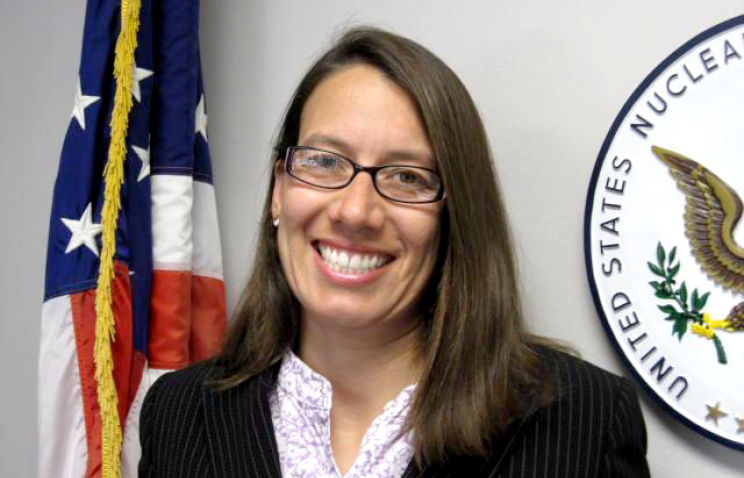 Laura Micewski poses in front of an American flag and U.S. Nuclear Regulatory Commission crest.