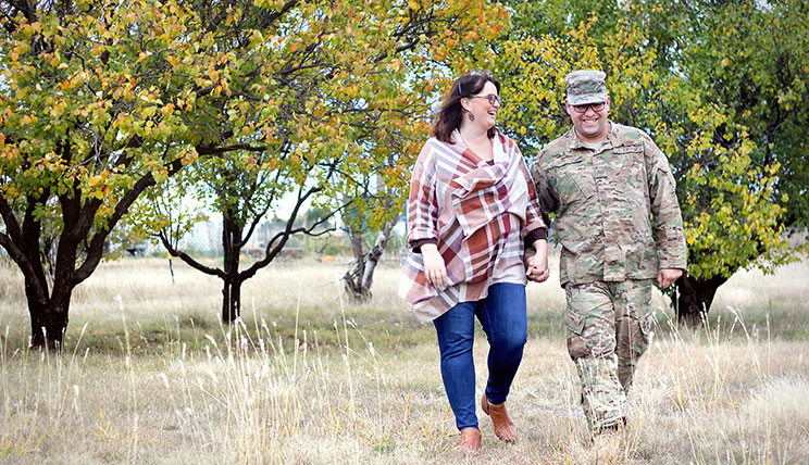 Janine Romero and her husband, Lee, walk through a dry grassy area holding hands.