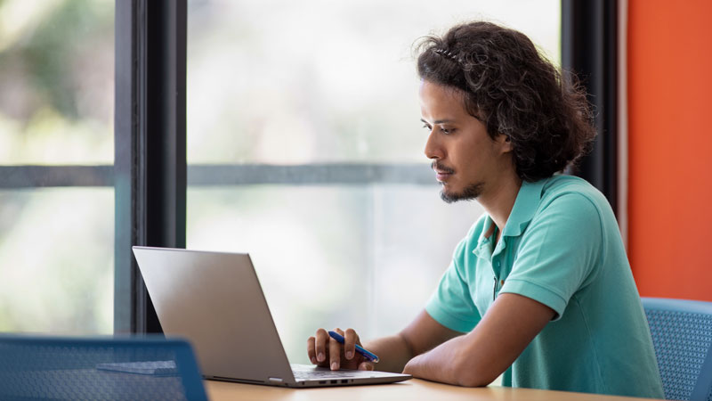 A student sits at a table while working on his laptop, a typical online learning environment