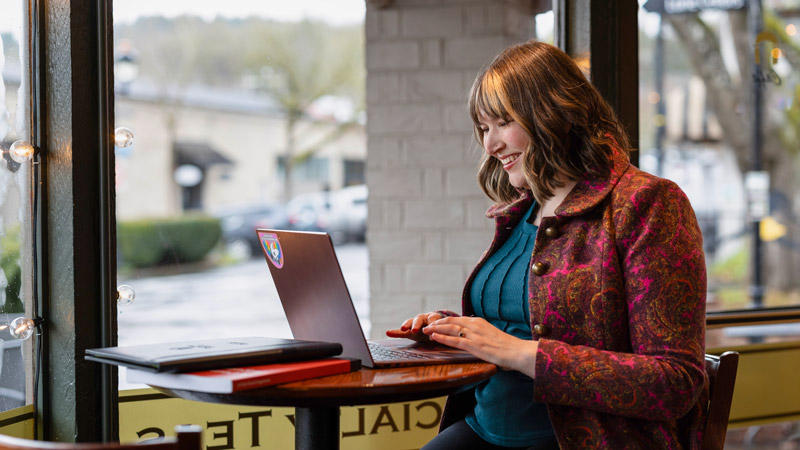 Oregon State student Kaitlin Lee types on a laptop while sitting in front of a sunny window.