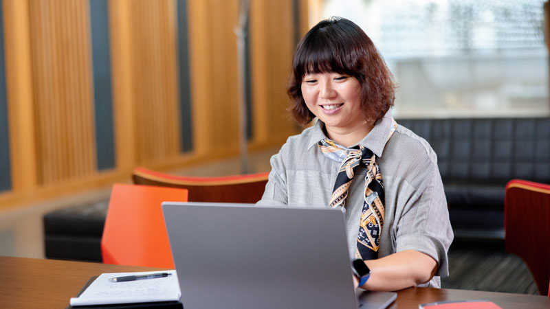 Ecampus psychology graduate, Karen Baek sits at a table, working at her laptop.