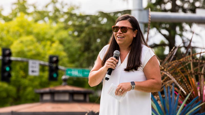 Beaverton mayor and Lacey Beaty speaks into a microphone at an outdoor public event.