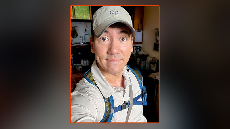 Marc Mains in baseball hat and backpack standing in office of Monteverde Institute