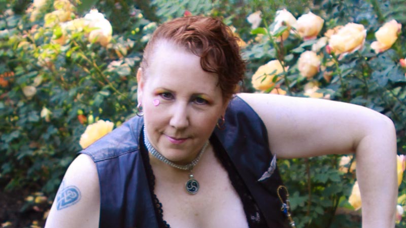 A person kneeling in a black vest with yellow roses behind them.