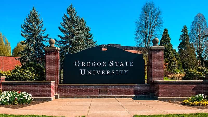 Scenic image of the black entrance sign to Oregon State University with trees in the background