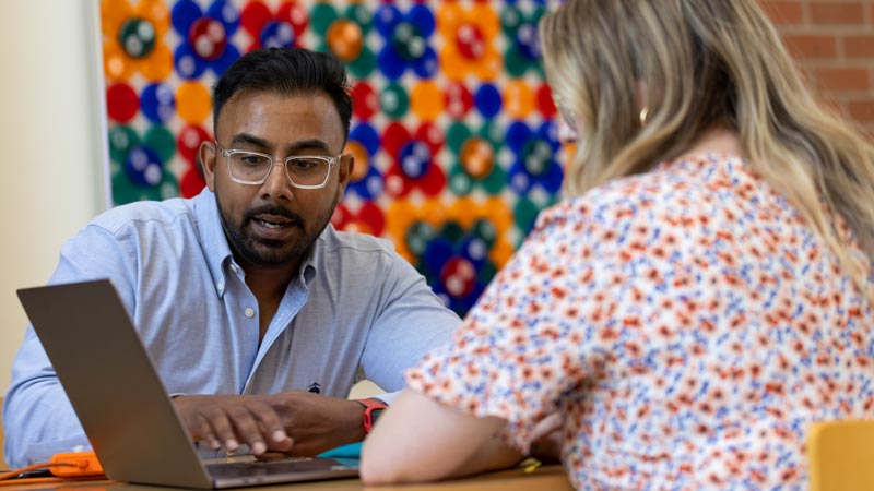 Two people talking over a laptop computer