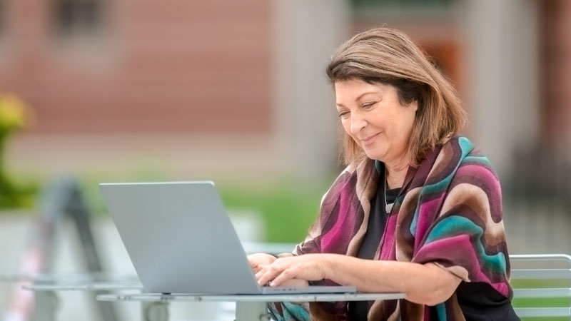 A woman works on a laptop computer while sitting at an outdoor table.