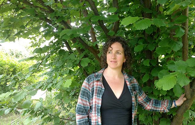 Oregon State Ecampus sociology alumna Sarah Brown stands with one hand resting on the branch of a tree.