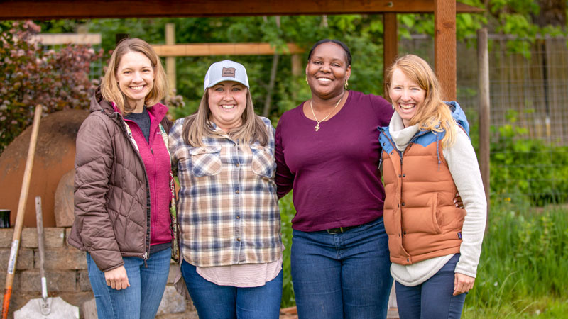 A group of four women stand together, smiling. From left to right, the women include Carolyn Breece, Melissa Milhollin, Velda Hendricks (Ecampus graduate) and Deanna Lloyd.