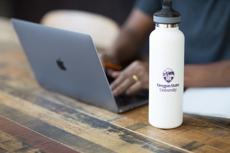 Student working on a laptop while seated at a table, with an Oregon State Ecampus water bottle in the foreground