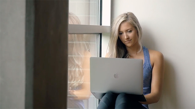 Calais Bickford-St. Pierre, an online environmental sciences alumna, sits on a large windowsill with a laptop on her knees.