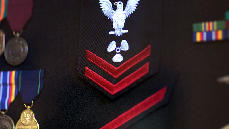 A U.S. Navy military uniform with badges and patches on the breast and sleeves.