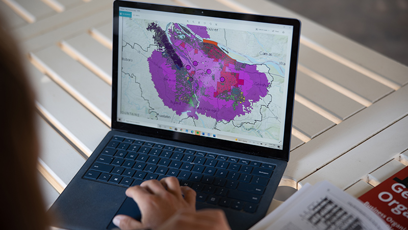 A person's hands rest on a laptop keyboard with a colorful geographic map displayed on the screen.