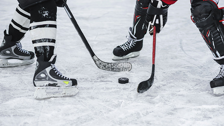 Hockey players face off with a puck on the ice between their sticks.