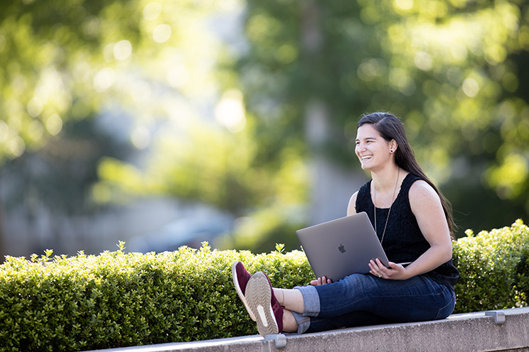 Hope Nelson sits on a concrete bench with a computer on her lap outside the Oregon State Valley Library. She earned an online German degree from OSU.