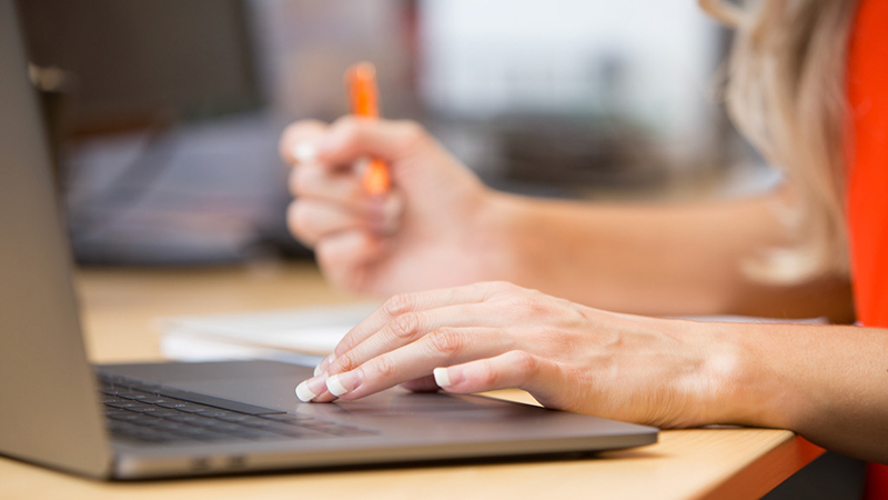 A person uses a laptop while writing with a pen in a notepad.