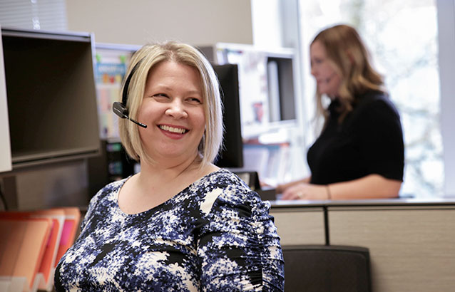 Two Ecampus enrollment specialists in an office space wearing phone headsets.