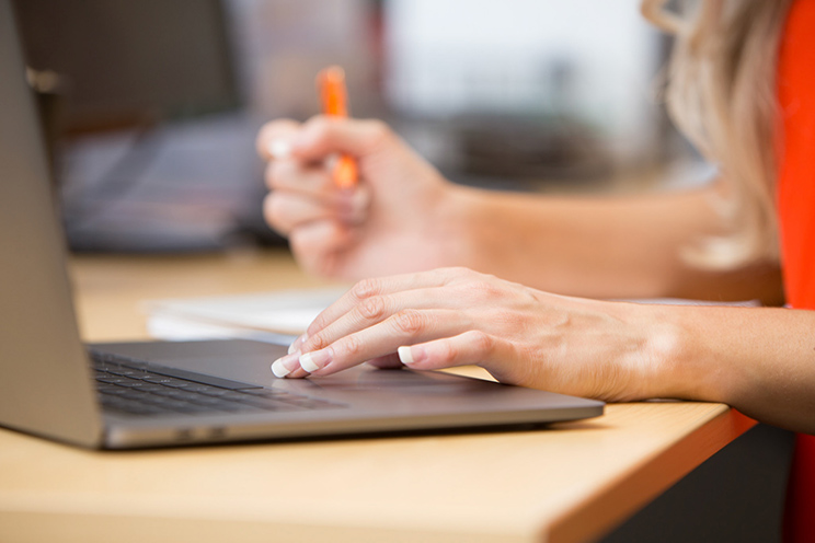 A woman uses a laptop while also writing on a notepad