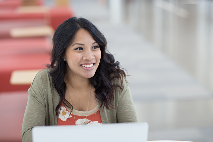 Oregon State Ecampus graduate Samantha Diaz sits at a table and uses a laptop. Tuition