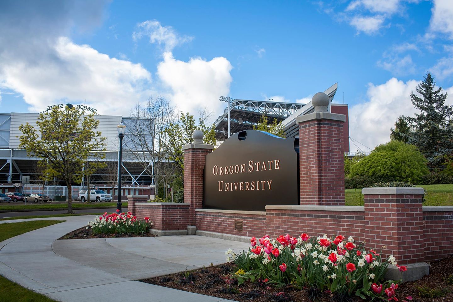 A black sign with gold lettering surrounded by a brick ledge and blooming flowers reads "Oregon State University," which is ranked #1 for best online liberal arts colleges