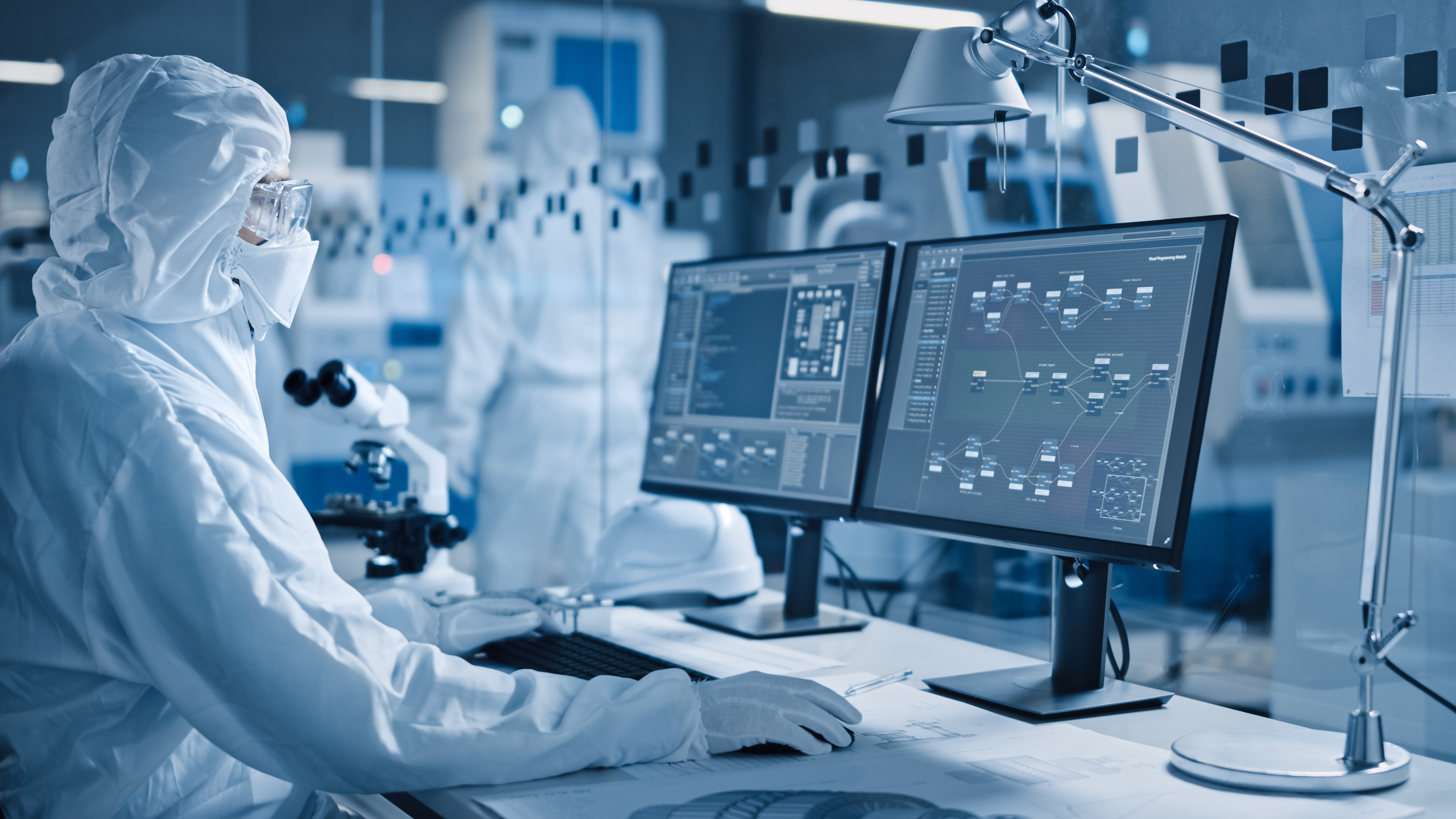 A person in a full-body suit works on a computer in a clean room.